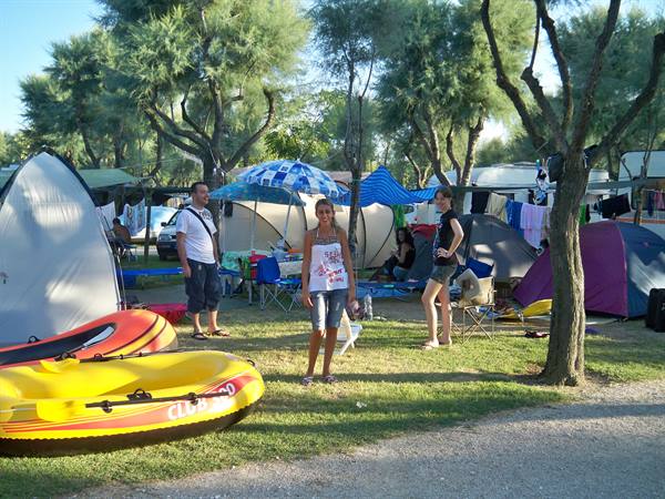 Campsite among trees: tents, umbrellas, yellow inflatable boats and holidaymakers in the sun