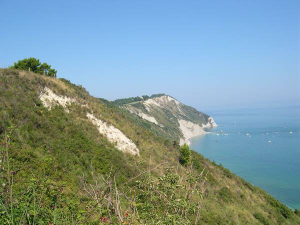 Conero coast: green slopes and limestone cliffs over blue sea with boats