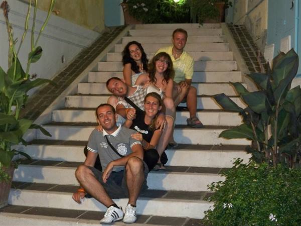 Six smiling friends sitting on a lit staircase at night among green plants