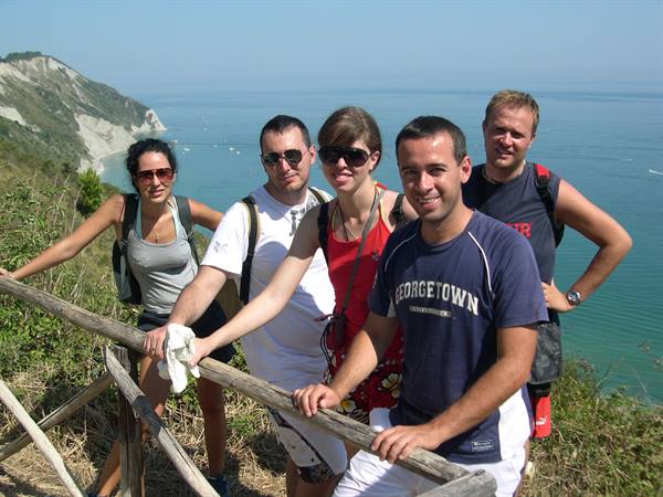 Hiking group with backpacks leaning on wooden fence above the blue sea