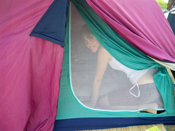 Smiling girl inside a pink and green tent, behind the mesh door