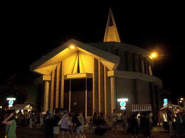 Modern church lit at night, crowd of people in the square