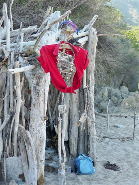 Driftwood skeleton wearing red shirt outside a beach hut on the sand
