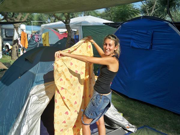 Smiling woman hangs a yellow sheet between tents at the campsite