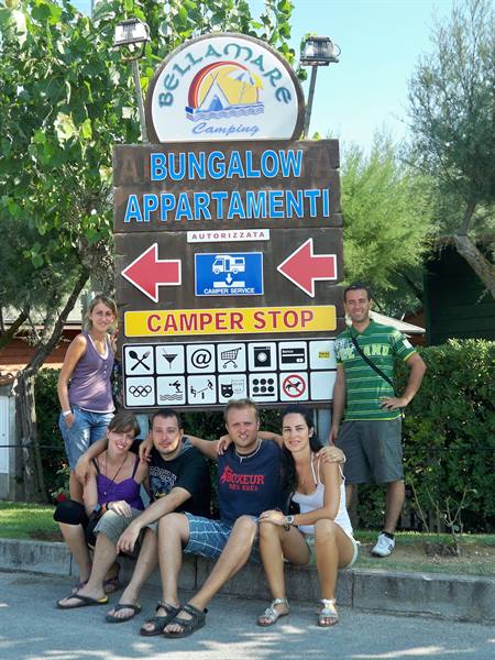 Friends posing by the wooden Bellamare camping sign, sunny day