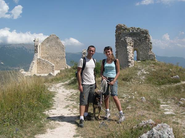 Two hikers with a dog on a trail among old stone ruins