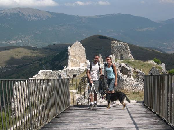 Couple with dog on wooden bridge before Rocca Calascio castle ruins