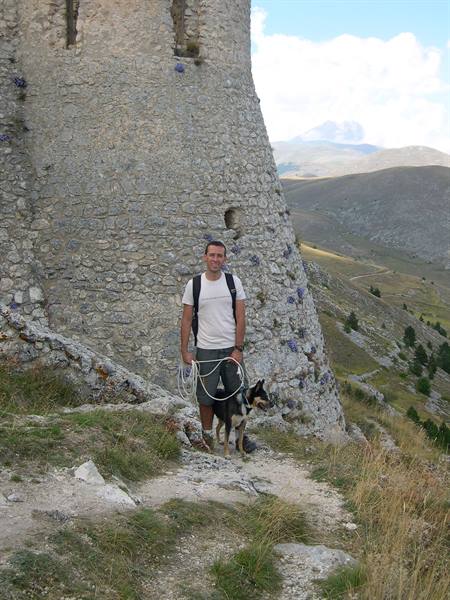 Hiker with dog beside a medieval stone tower at Rocca Calascio
