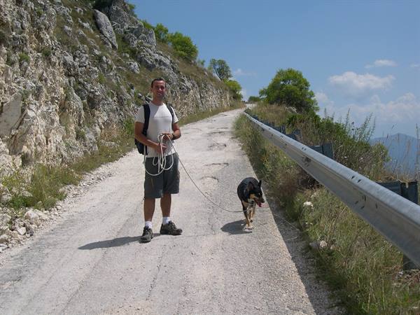 Man with backpack and leash walks his dog on a white gravel mountain road