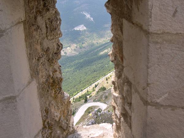 White winding road through green mountain woods seen through a stone arrow slit