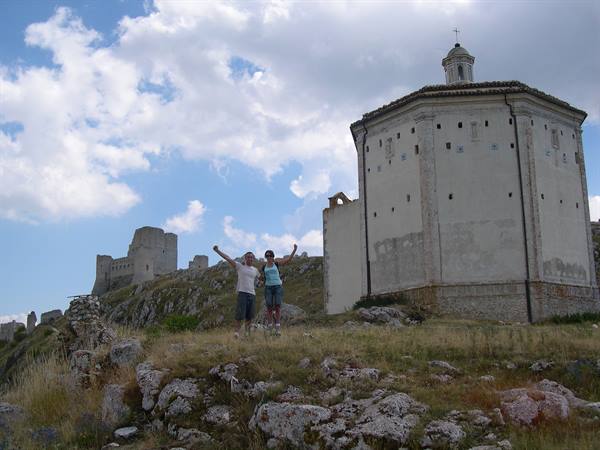 Two hikers raising arms near Santa Maria della Pietà church, Rocca Calascio