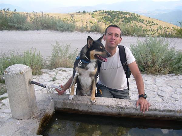 Man with backpack and dog by a stone mountain fountain