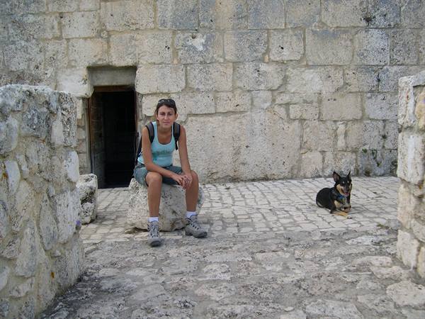 Girl with backpack sitting on a boulder by stone walls, small dog nearby