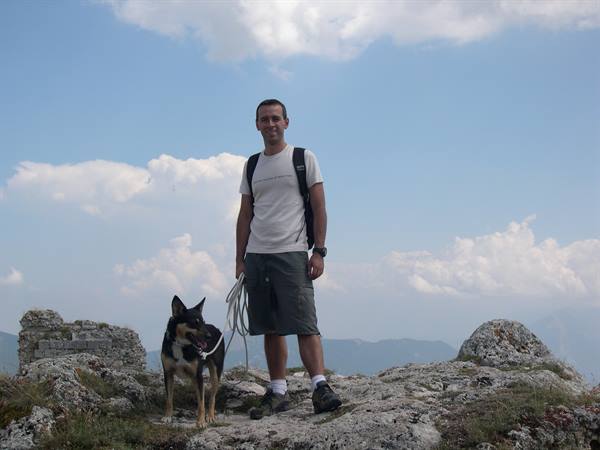 Hiker with backpack and leashed dog on limestone rocks in the mountains