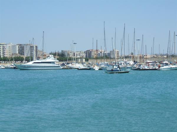 Yachts and sailboats moored in the marina, buildings on the shore, turquoise water