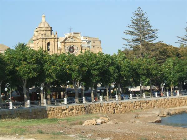 Baroque church with dome and clock behind trees along the seafront