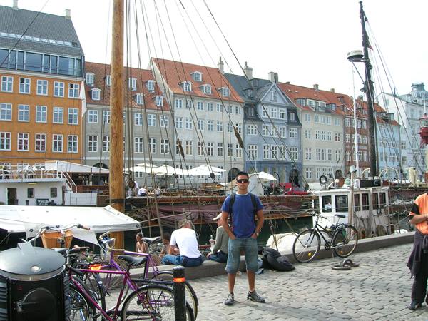 Tourist in blue shirt on Nyhavn waterfront among bicycles and old wooden sailing ships