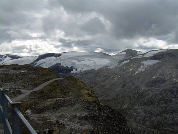 Road with railing leading to a glacier among rocky mountains, cloudy sky