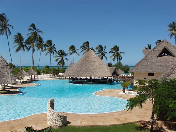 Blue swimming pool among palms and thatched-roof bungalows at the resort
