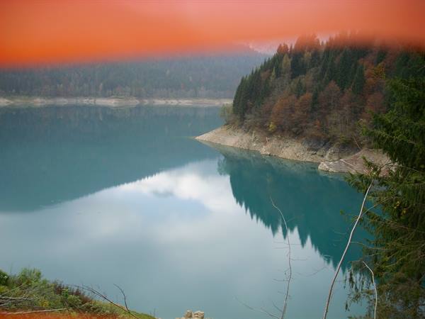 Turquoise lake surrounded by autumn conifers, rocky shores and sky reflected on the water