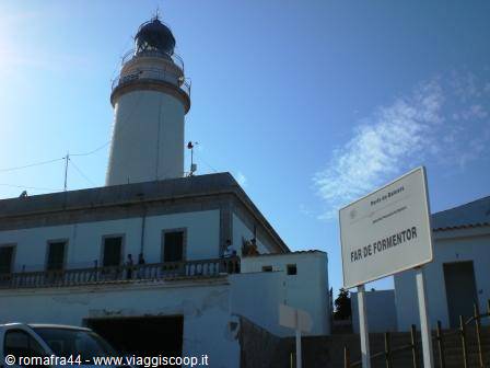 White Formentor lighthouse with sign, tourists on terrace under sun