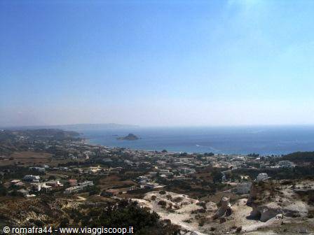 Whitewashed coastal town, scattered houses, blue sea with small islands, bright sunlight