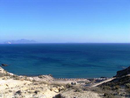 Sandy beach beneath arid cliffs, turquoise sea and distant islands