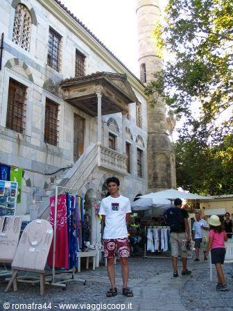Tourist in front of an old stone mosque with minaret, open-air market