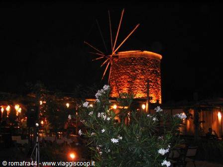 Stone windmill lit up at night, motionless sails, white flowers in foreground