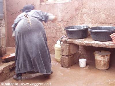 Woman bends washing in earthen courtyard, black basins on stone bench