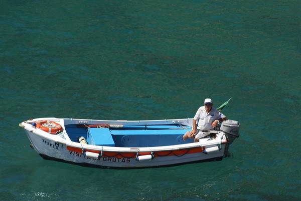 Fisherman in white and blue boat on emerald green sea