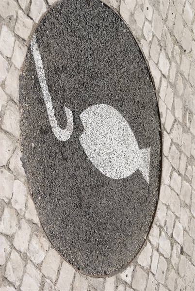 Fish and hook sign painted on asphalt among cobblestones
