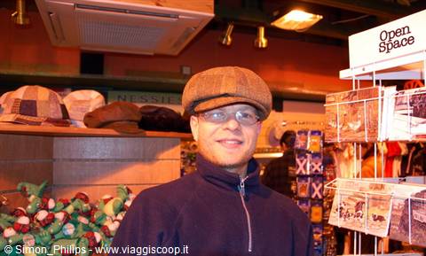 Man wearing tweed flat cap and glasses inside a souvenir shop