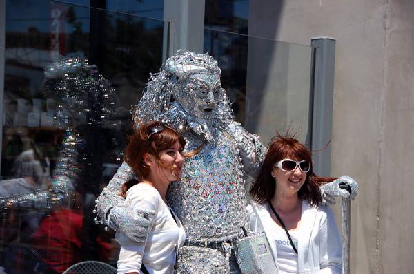 Silver living statue with outstretched arms hugging two smiling women on the street