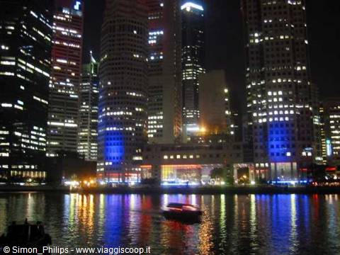 Illuminated skyscrapers reflected on bay water, a boat passing at night, Singapore