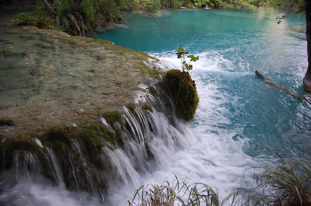 Small waterfall over mossy travertine in the turquoise water of Plitvice Lakes