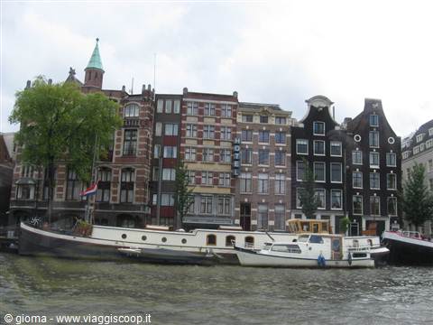 Amsterdam canal houses with narrow facades and hotel sign, boats moored along the water