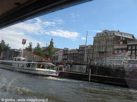 Tour boat on Amsterdam canal, historic houses and bridge under blue sky