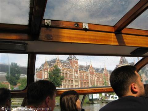 Tourists under the boat's wooden roof, Amsterdam Centraal station across the canal