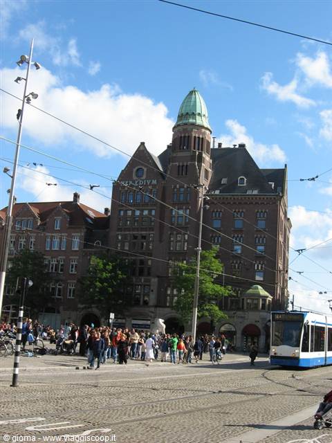 Blue tram on tracks in front of the Hotel American in Amsterdam, crowd under blue sky
