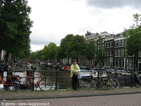 Woman in green jacket beside bicycles on a bridge over an Amsterdam canal