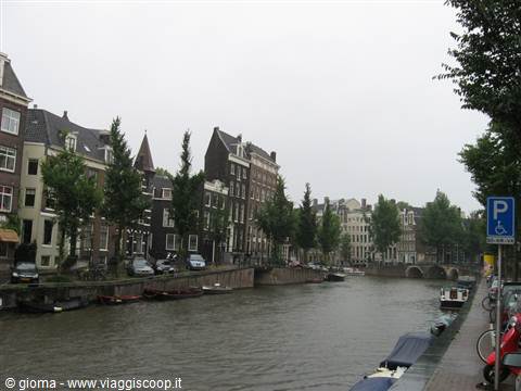 Tall canal houses in Amsterdam, moored boats, grey sky