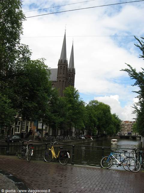 Bikes parked on a bridge by the canal near the Krijtberg church spires, Amsterdam