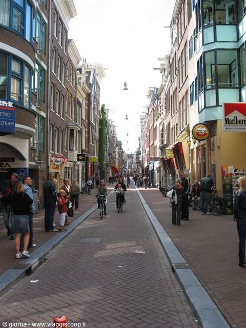 Cyclists and pedestrians on a cobbled shopping street lined with Amsterdam houses