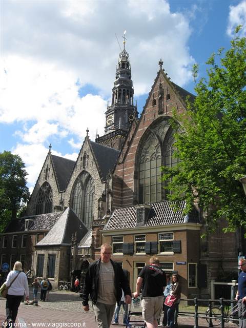 Oude Kerk in Amsterdam, brick Gothic facade with tall stained-glass windows, tourists walking by