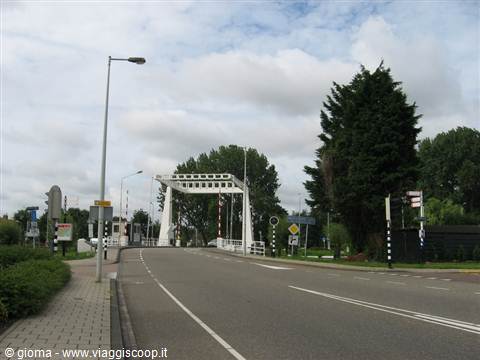 White metal drawbridge over an asphalt road, trees and cloudy sky