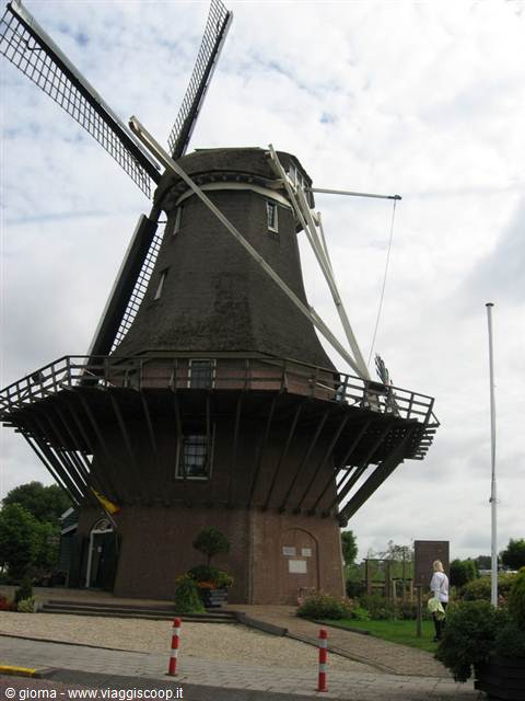 Dutch brick and wooden windmill under cloudy sky, tourist on the path