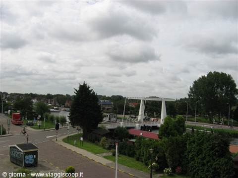 White drawbridge over the canal, houses and trees under cloudy sky