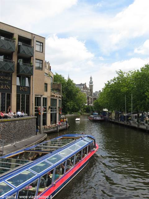 Glass-roofed tourist boat cruising a canal lined with pubs and Dutch houses