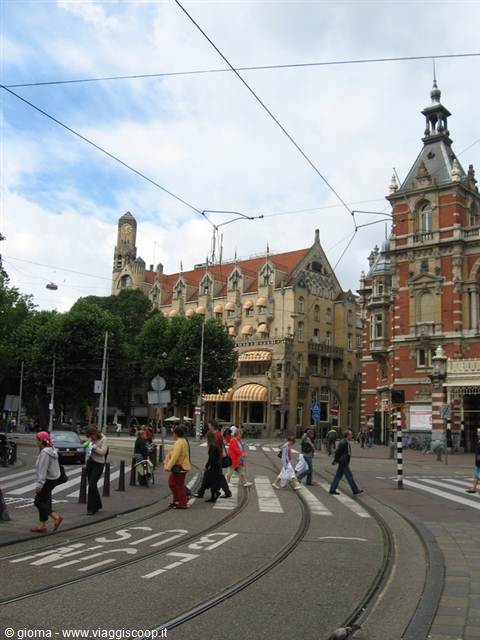 Pedestrians cross tram tracks in Amsterdam under red brick buildings